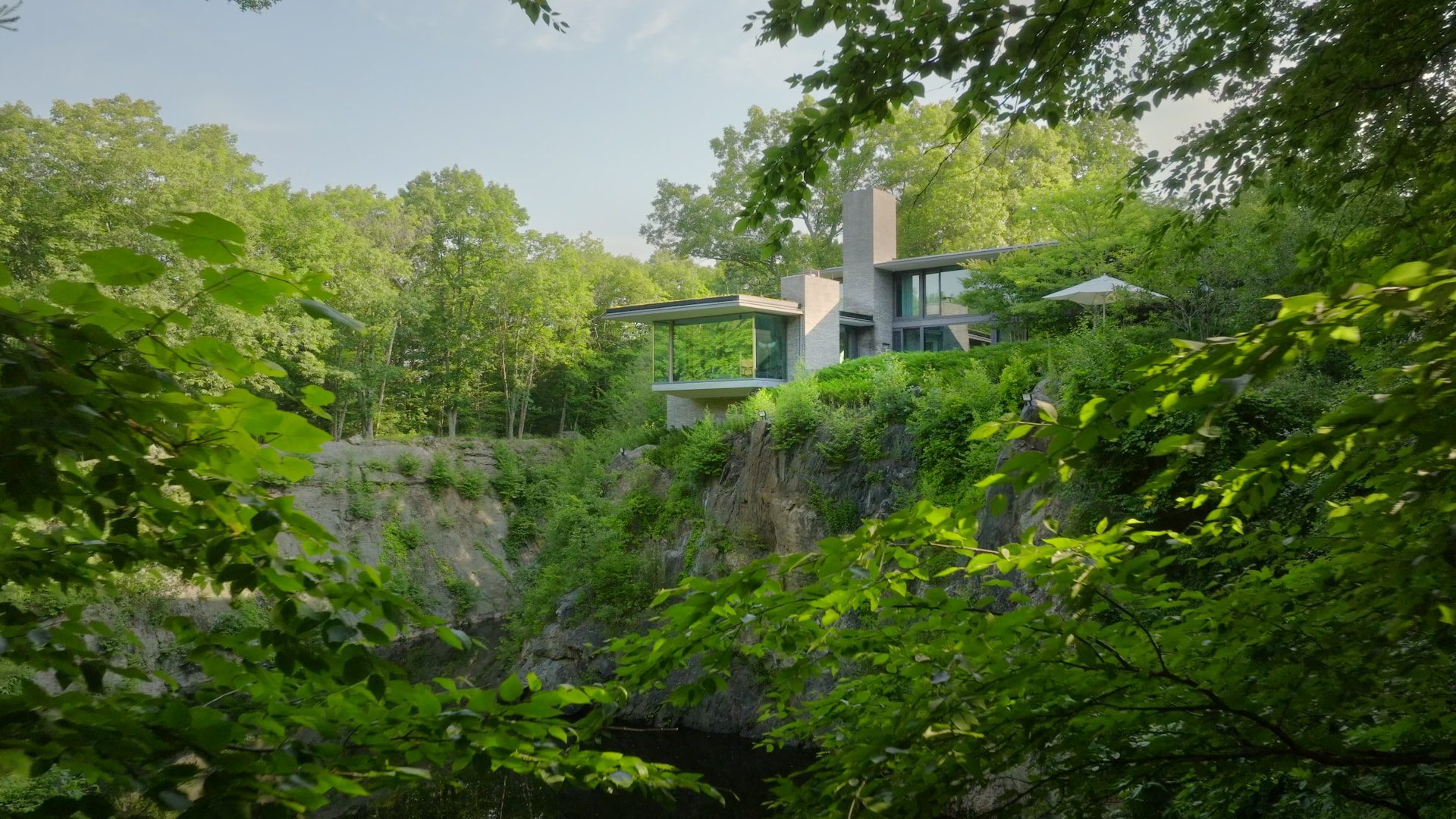 Bedford Quarry — glass and stone house cantilevered above the quarry face, framed by summer foliage